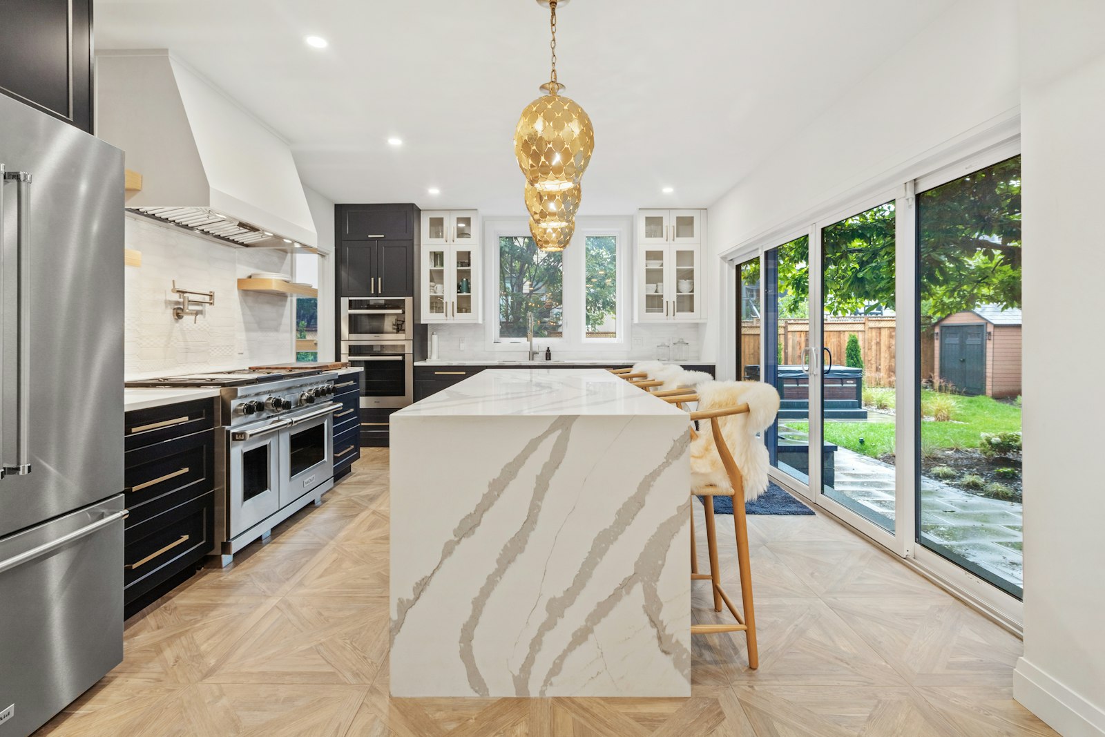 A kitchen with a marble island and brass pendant, open to the garden